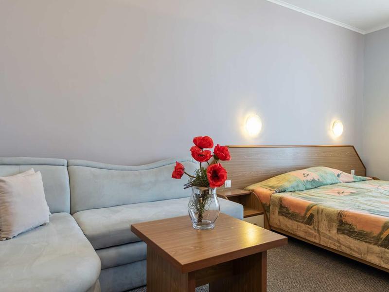 Cozy hotel room with double bed, sofa, table, and vase of flowers.
