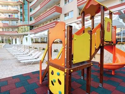 Colorful children's playground with slide next to sun loungers in a hotel courtyard.