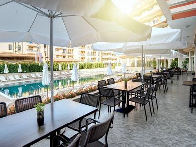 Outdoor hotel area with tables, chairs, umbrellas next to a pool.
