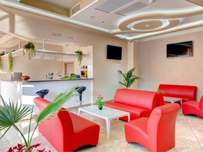 Bright hotel lounge area with red chairs, white table, and reception desk in the background.