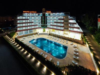Hotel building with illuminated pool at night, surrounded by sun loungers.