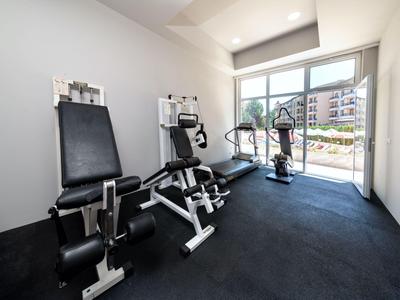 Pequeño gimnasio con máquinas de entrenamiento, grandes ventanas y vista al patio.