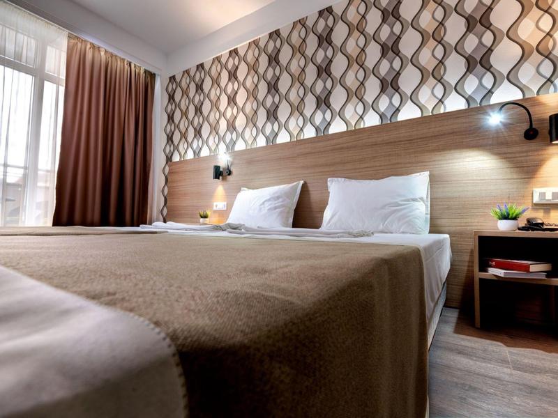 A modern hotel room with a large bed, patterned walls, and bedside tables.