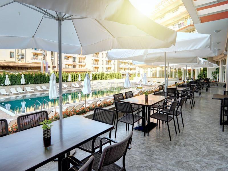 Outdoor hotel area with tables, chairs, umbrellas next to a pool.