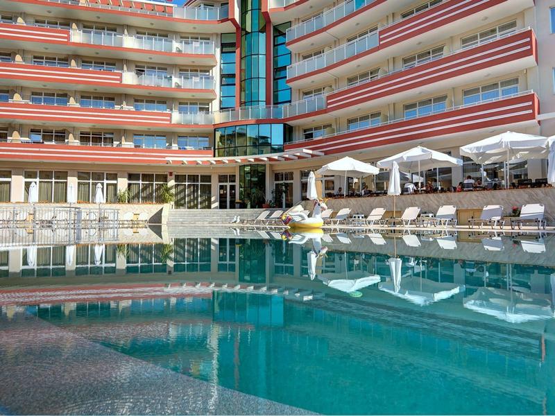 Modern hotel pool with lounge chairs and umbrellas in front of a large building.