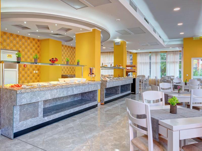 Bright hotel restaurant with yellow walls, marble buffet, and white tables with chairs.