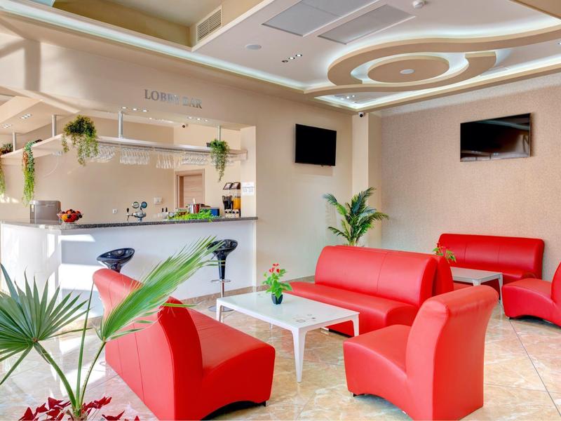 Bright hotel lounge area with red chairs, white table, and reception desk in the background.
