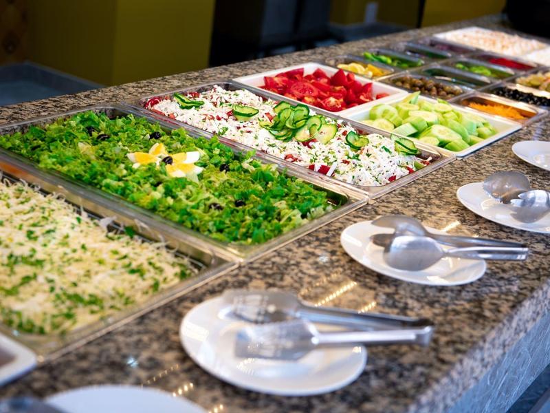 Buffet with various fresh salads in rectangular bowls on a gray marble countertop.