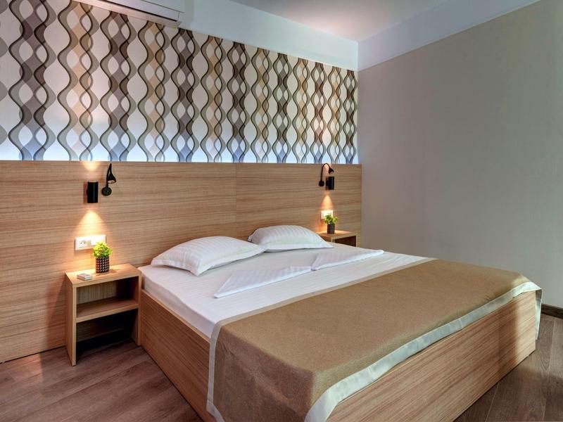 Cozy double bed with brown bedspread and nightstands in a modern hotel room.