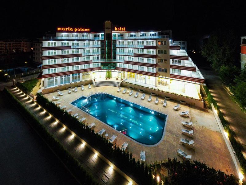 Hotel building with illuminated pool at night, surrounded by sun loungers.