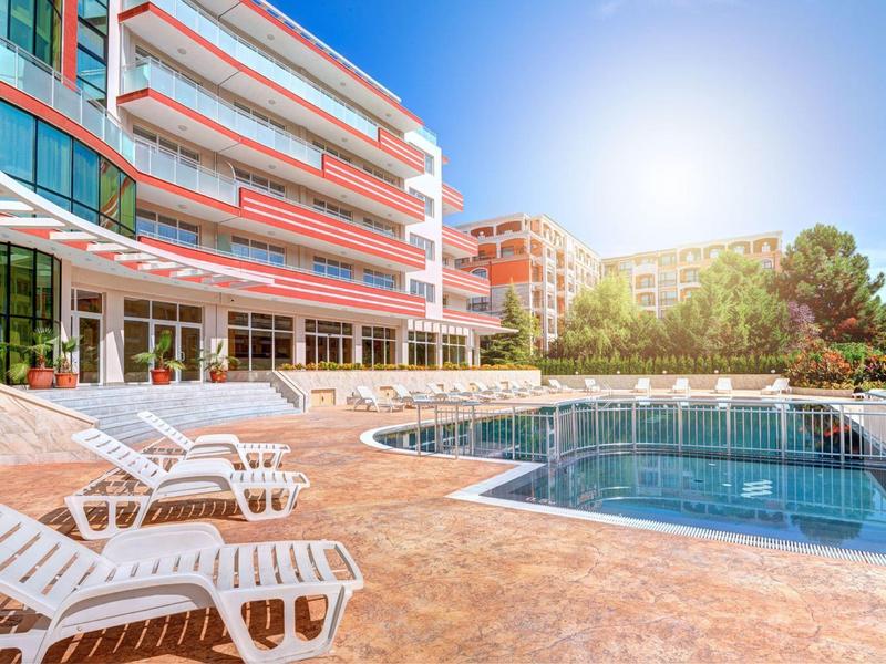 Hotel with outdoor pool, lounge chairs, and sunny sky in late afternoon.