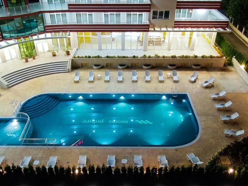 Illuminated hotel swimming pool with lounge chairs and seating areas on the terrace at night.