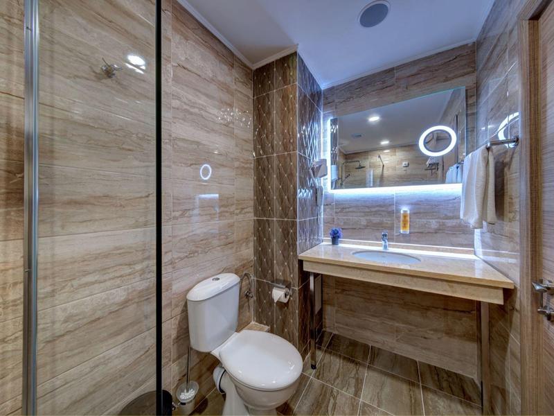 Modern bathroom with illuminated mirror, toilet, and shower cabin featuring wood-look tiles.