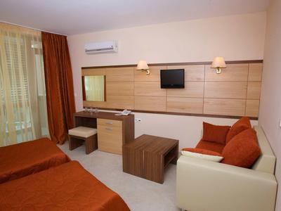 Modern hotel room with two beds, sofa, desk, and wall-mounted TV.