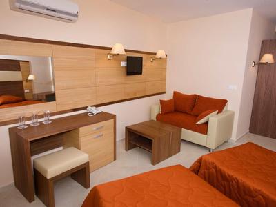 Hotel room with two beds, sofa, desk, and wall mirror in warm tones.