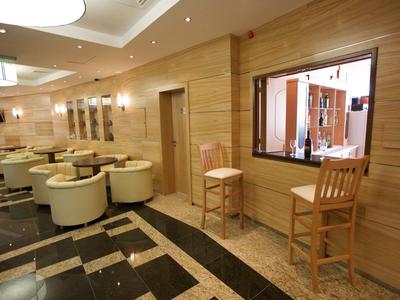 Modern hotel lounge with leather chairs, wooden walls, and a service counter with two wooden chairs.