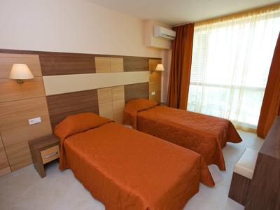 Two single beds with orange bedspreads in a bright hotel room with large window.