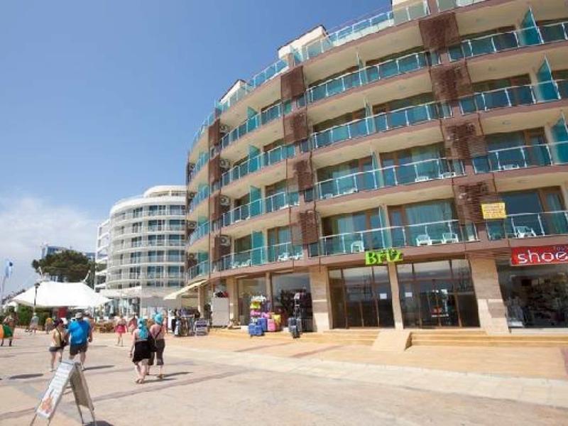Multi-story hotel building with balconies and a busy walkway under clear sky.