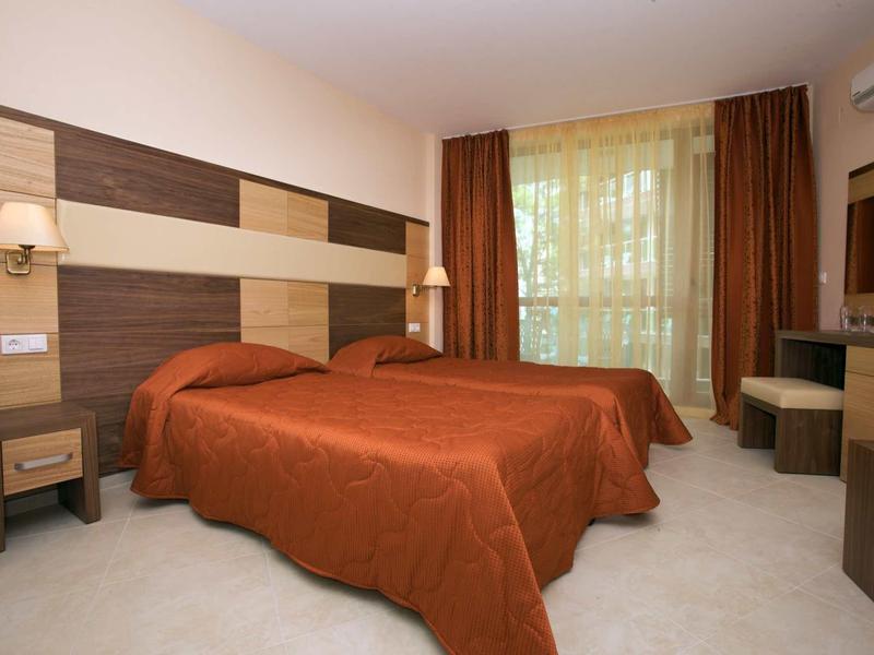 Hotel room with two single beds, orange bedspreads, and a desk by a large window.