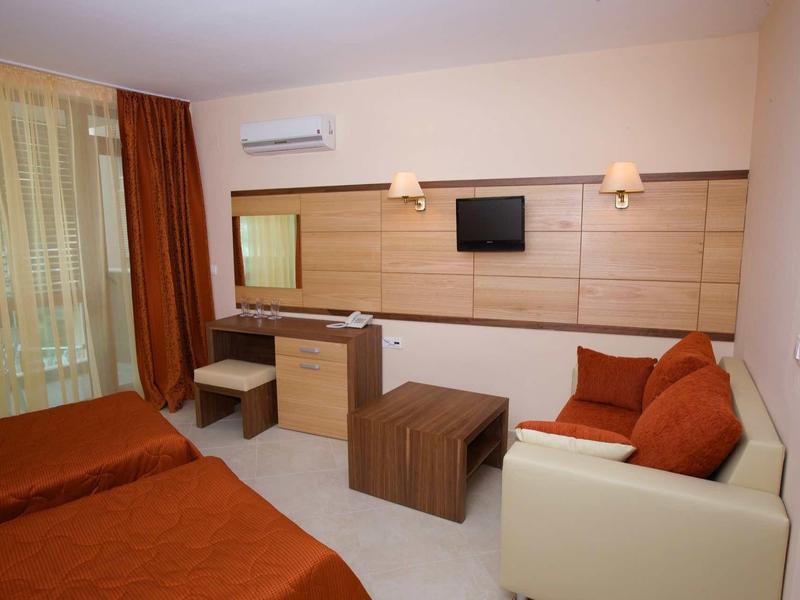 Modern hotel room with two beds, sofa, desk, and wall-mounted TV.