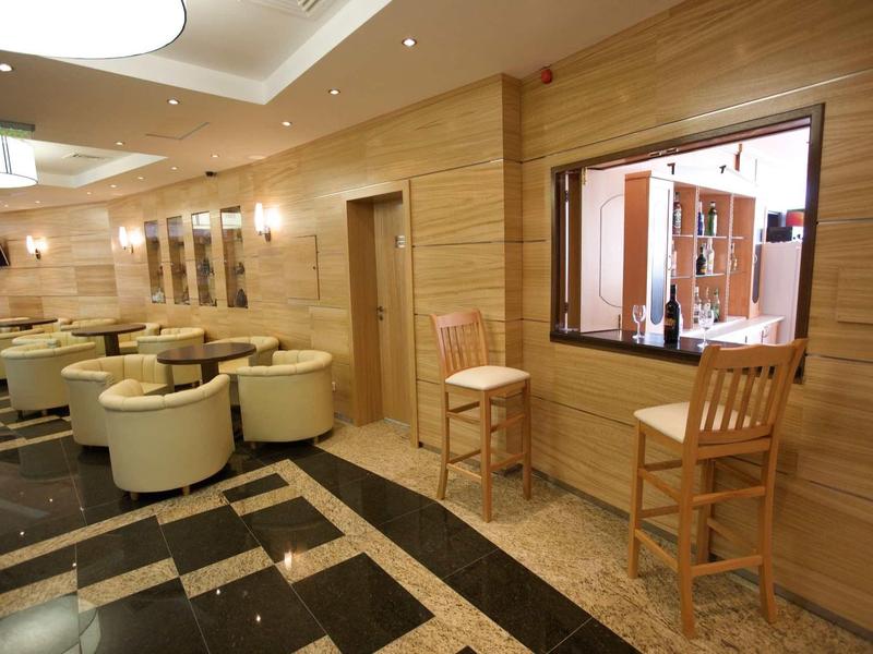 Modern hotel lounge with leather chairs, wooden walls, and a service counter with two wooden chairs.