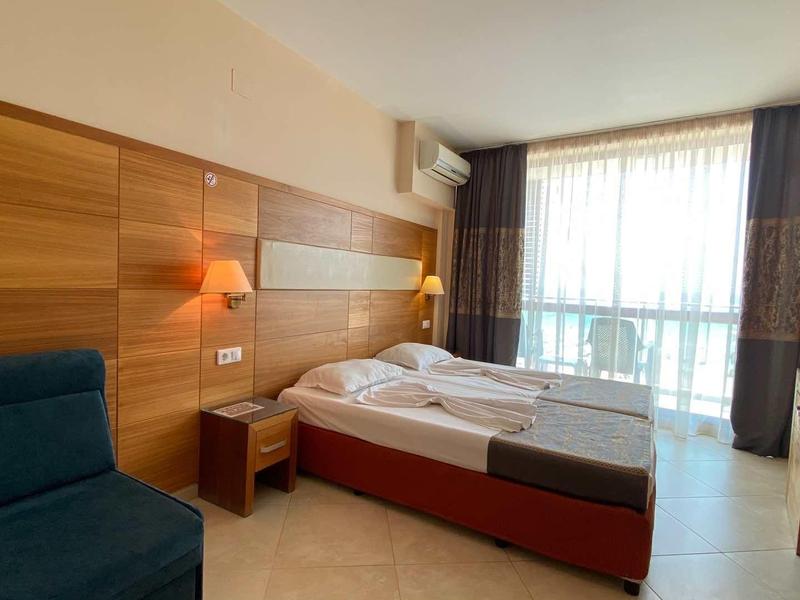 Bright hotel room with large window, single bed, blue sofa, and wooden wall accents.