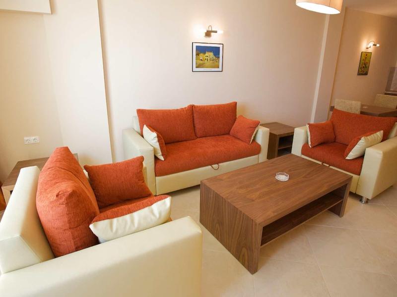 Bright living room with two white sofas with orange cushions and a wooden table.