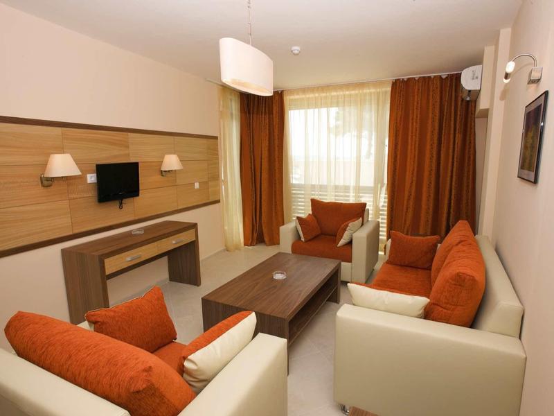 Modern living room with white armchairs, orange cushions, and large window with brown curtains.