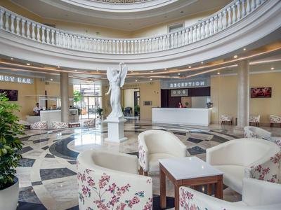 Helle Hotellobby mit weißem Rundbau, Marmorboden und bequemen Sesseln mit floralem Muster.