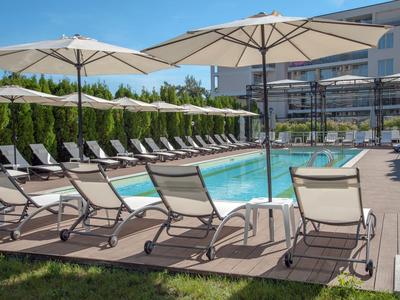Zwembadgebied met ligstoelen en parasols naast een hotel onder een blauwe lucht.