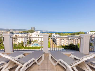 Uitzicht vanaf een terras met ligstoelen op stadsgebouwen en de zee in de verte.