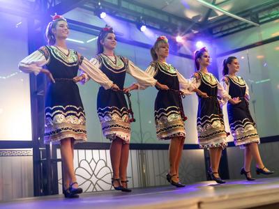 Vijf vrouwen in traditionele kostuums dansen op een podium met verlichting.