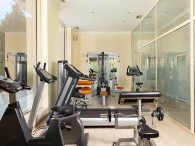 Lichte fitnessruimte met trainingsapparatuur en grote glazen ramen.