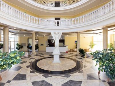 Elegante hotellobby met marmeren vloer en centraal beeld onder een koepel.