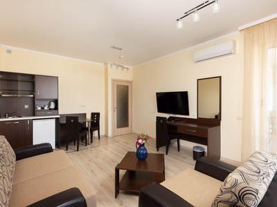 Lichte hotel-lounge met zithoek, tv, kleine keuken en eettafel.