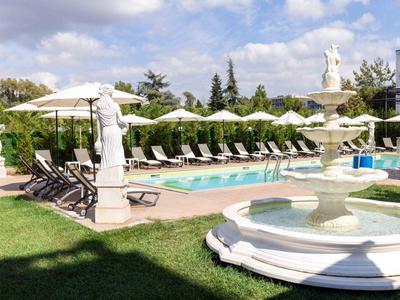 Zwembadgebied met standbeelden, ligstoelen en parasols in een hotel tuin