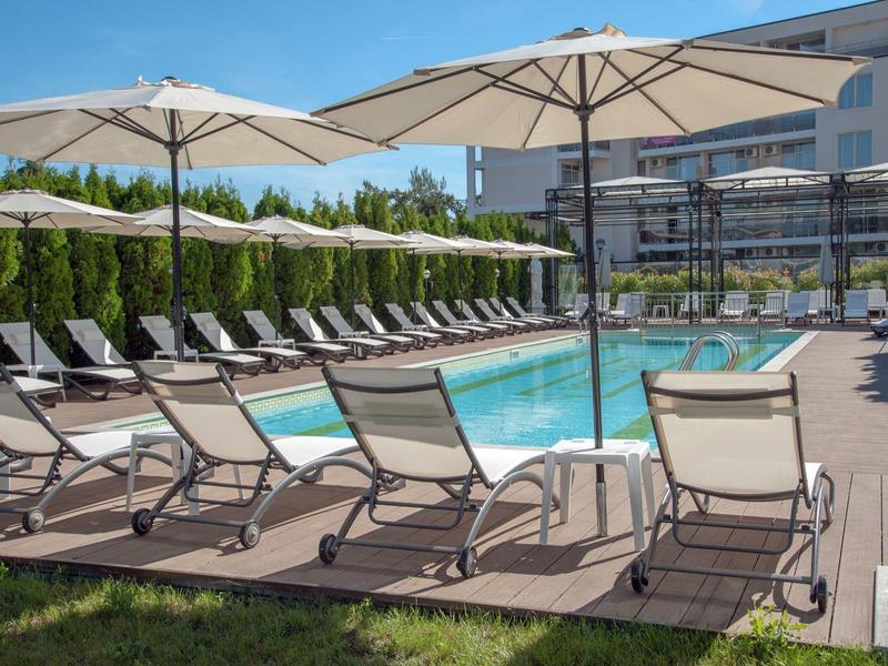 Modern hotelzwembad met ligstoelen en parasols onder een heldere blauwe lucht.