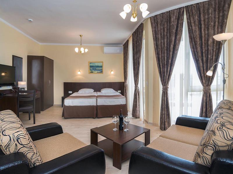 Elegante hotelkamer met tweepersoonsbed, zithoek en grote ramen met gordijnen.