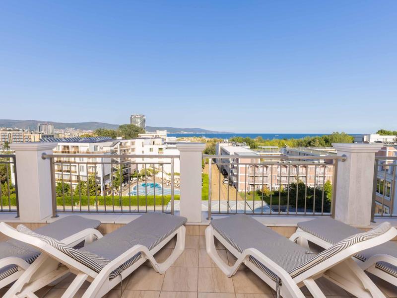 Uitzicht vanaf een terras met ligstoelen op stadsgebouwen en de zee in de verte.