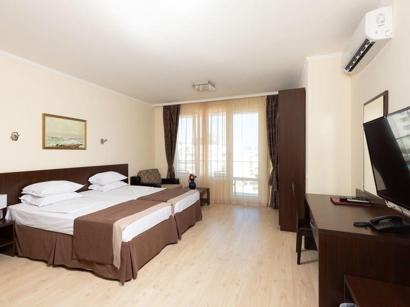 Lichte hotelkamer met twee eenpersoonsbedden, tv, bureau en balkon met gordijnen.