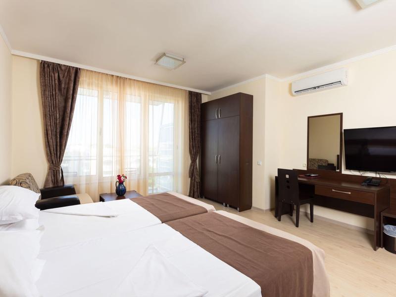 Modern hotelkamer met tweepersoonsbed, flatscreen-tv en balkon met gordijnen.