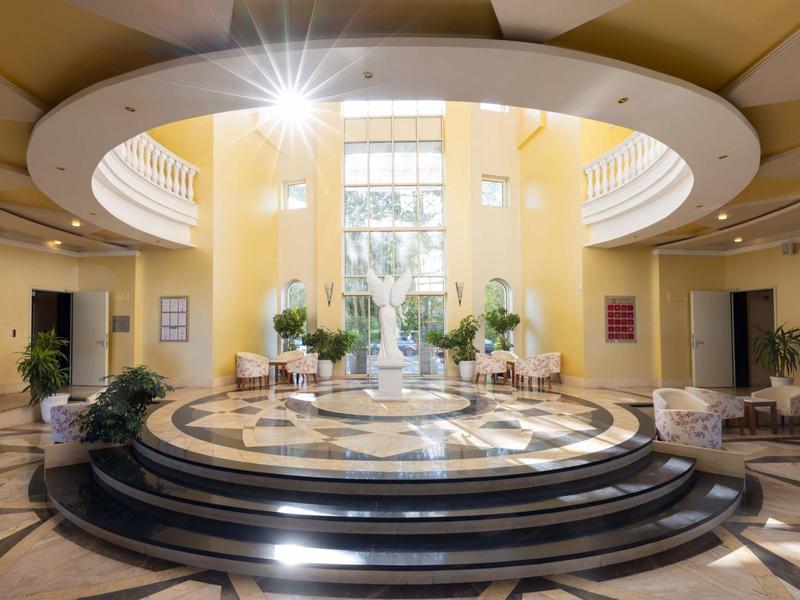 Lichte hotel lobby met ronde trap, marmeren vloer en grote glazen voorkant.