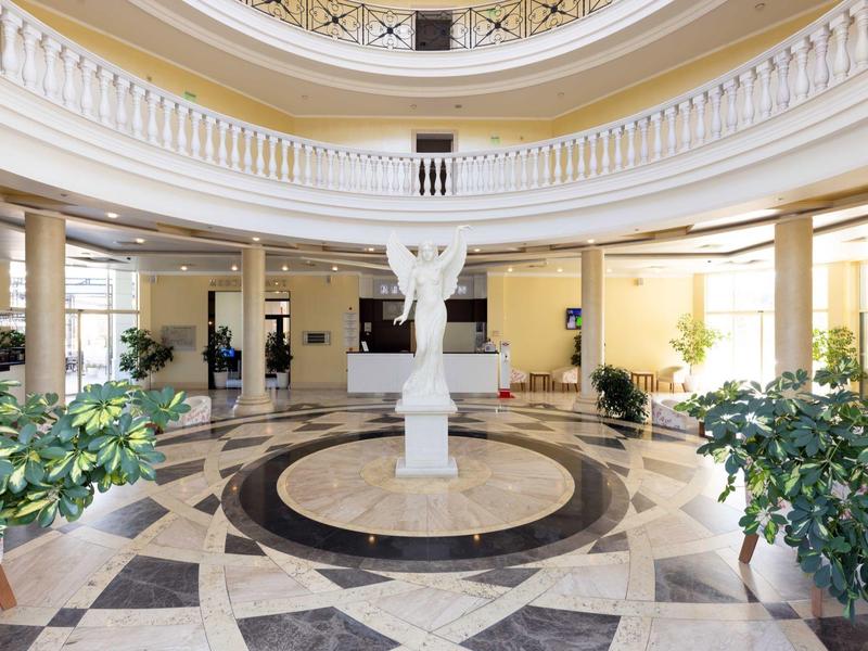 Elegante hotellobby met marmeren vloer en centraal beeld onder een koepel.