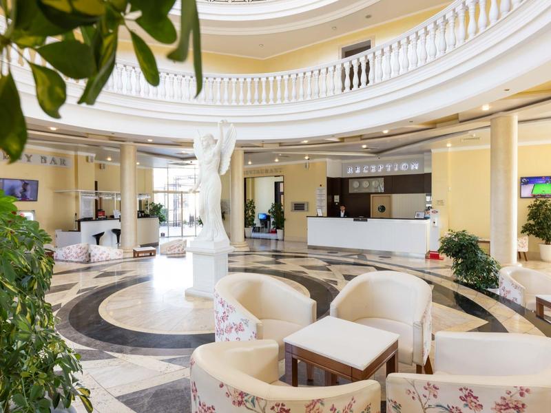 Lichte hotellobby met ronde plafond, wit meubilair en receptiebalie op de achtergrond.