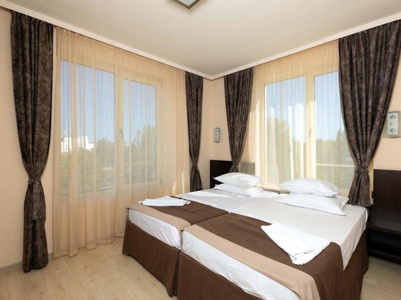 Gezellige hotelkamer met een tweepersoonsbed, bruine gordijnen en lichte houten vloer.