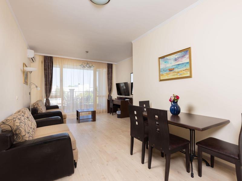 Lichte woonkamer met bank, eettafel, stoelen, tv en groot raam met gordijnen.