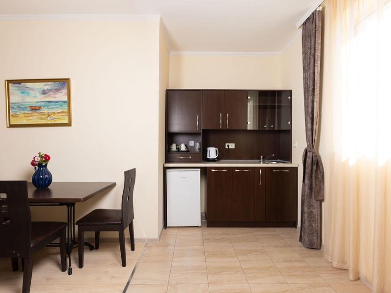 Kleine hotelkeuken met donker meubilair, mini-koelkast en eettafel met stoelen.