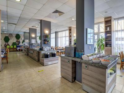 Moderner Gastraum mit hellen Wänden, großen Fenstern, Holz- und Steinelementen, Buffet und Stühlen.