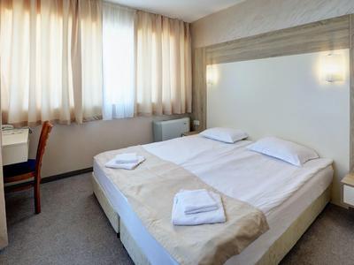 Kleines helles Schlafzimmer mit Doppelbett, weißen Bettlaken, Handtüchern und einem Schreibtisch am Fenster.