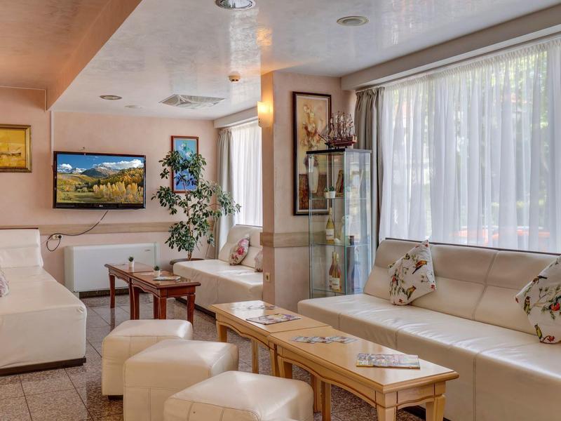 Helles Wohnzimmer mit weißen Polstermöbeln, Holztischen, großen Fenstern und warmen Lichtquellen.